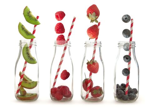 Berry fruits and kiwi falling into glass bottles with straws over a white background