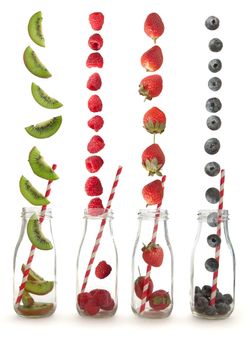 Berry fruits and kiwi falling into glass bottles with straws over a white background