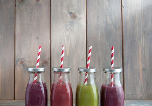 Flavoured smoothies in bottles in a rack over a wooden background with copyspace