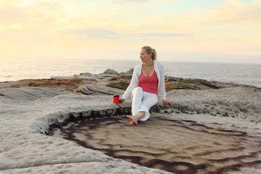 A woman relaxes by the ocean enjoying her morning coffee