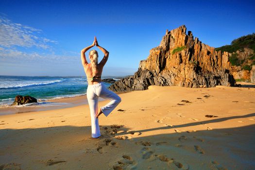 Female stretching on one leg yoga tree pose vrksasana by the beach early morning