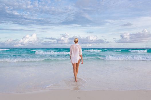 Woman wearing white loose tunic over bikini on Mahe Island, Seychelles. Summer vacations on picture perfect tropical beach concept.