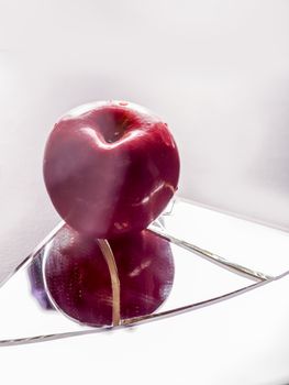 Red apple on cracked broken mirror reflecting