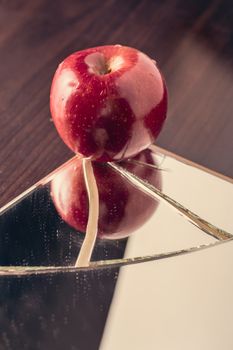 Red apple on cracked broken mirror reflecting