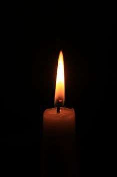 Single burning candle, close-up in the dark