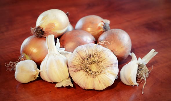 Garlics and onions heap on brown wooden table.