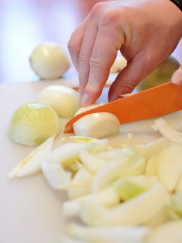 Hand holding orange ceramic knife and slicing the fresh onion into small pieces on cutting board.