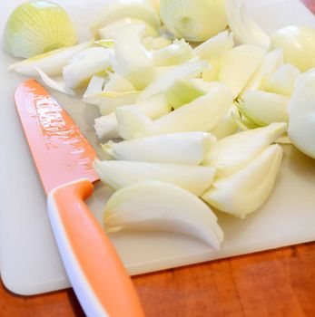 Chopped onion and orange ceramic knife on white cutting board. 