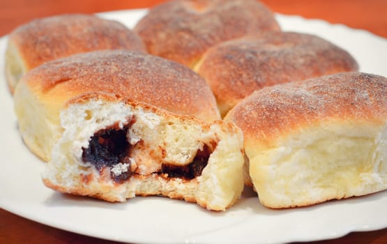 Buns filled plum jam. Bun with first missing bite on white plate.