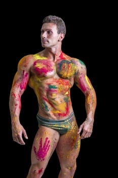 Muscular young man shirtless with skin painted with Holi colors, looking down, isolated on white