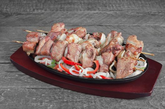 Grilled pork with lemon, salad of sweet peppers and onions in a cast iron pan grey wooden background.