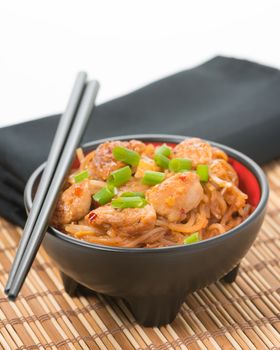 Spicy chicken pad thai in a black bowl on a bamboo placemat.