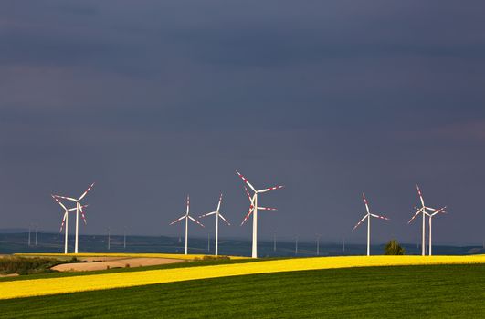 Green and yellow fields with Wind turbines generating electricity. Wind turbines before the thunderstorm. Spring sunny day on green field with wind power generators in Austria