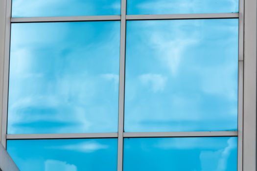Beautiful glass building facade with reflections from a blue sky and cloud formations.