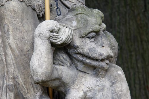 Baroque statue on the crossroad - Saint Procopius with bound devil.
Saint Procopius of Sazava (end of the 10th century Chotoun - March 25, 1053, Sazava) was originally a secular priest, later a hermit, co-founder and first abbot of the monastery Sazava. He was canonized in 1204. 
His main attribute is bound devil, which is at his feet or on which he stands.
Czech republic.