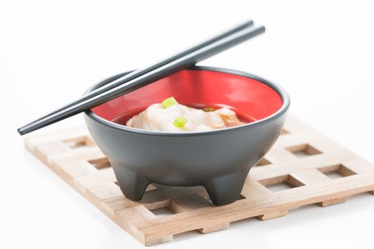 Wonton soup served in a black bowl on a wooden trivet.