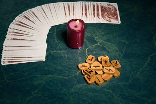 Composition of esoteric objects,candle,Cards and  wooden runes used for healing and fortune-telling,on green background,vintage style.