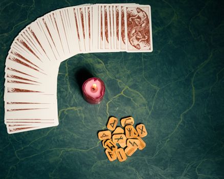 Composition of esoteric objects,candle,Cards and  wooden runes used for healing and fortune-telling,on green background,vintage style.View from above.