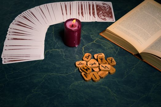 Composition of esoteric objects,candle,Cards,book and  wooden runes used for healing and fortune-telling,on green background,vintage style.