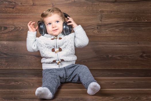 Baby boy looking up on wooden background with bluetooth/wireless headphones.