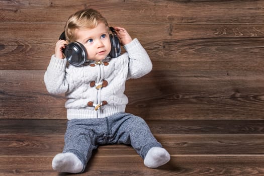 Baby boy looking up on wooden background with bluetooth/wireless headphones.