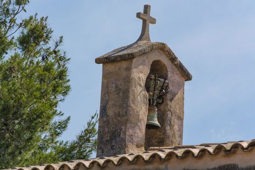 Church tower with bell in Spanish style against a blue sky.