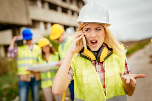 Beautiful young female construction architects using phone in front building damaged in the disaster.