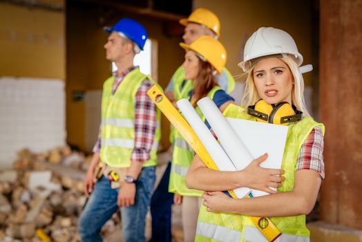 Beautiful young female construction architects at a construction site. She is holding plans and looking at camera.