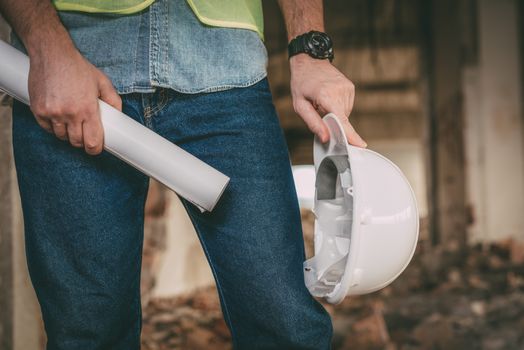 Close-up of a construction architects with white helmet and plans at construction site.