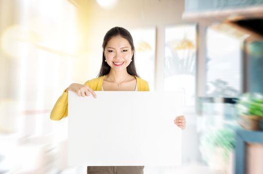 Young Asian woman hand holding a blank white paper card standing in her cafe. Copy space ready for text.