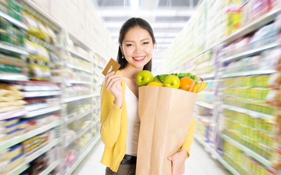 Young Asian woman hand holding shopping paper bag filled with fruits and vegetables and credit card in market or department store. 