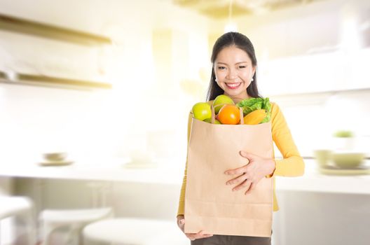 Young Asian woman hand holding shopping paper bag filled with fruits and vegetables in kitchen. 