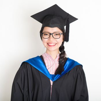 Happy university student in graduation gown and cap. Portrait of east  Asian female model standing on plain background.