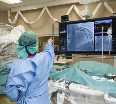 A surgeon with his back to the camera is pointing to a monitor during surgery in modern hospital.
