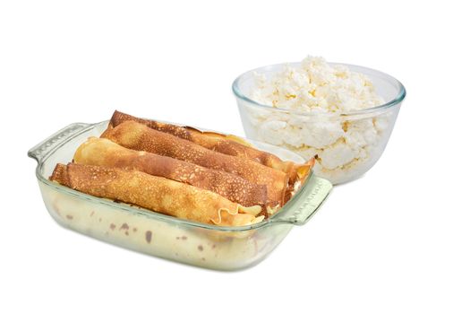 Pancakes filled with cottage cheese in the rectangular glass roasting pan and glass bowl with fresh cottage cheese on a light background
