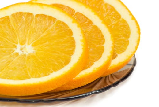 Fragment of several slices of an fresh orange closeup on a glass saucer on a light background
