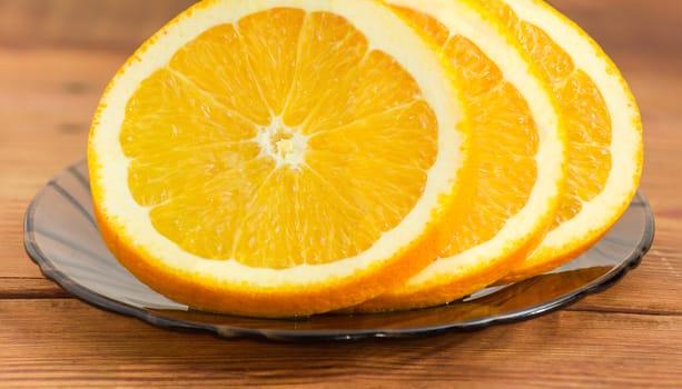 Several slices of an fresh orange closeup on a glass saucer on the wooden surface
