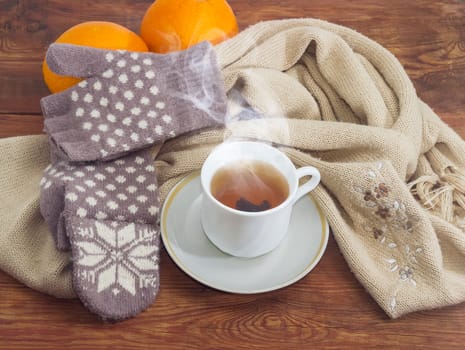 Cup of black tea on a background of women's woolen hybrid mittens and knitted scarf and oranges on wooden surface
