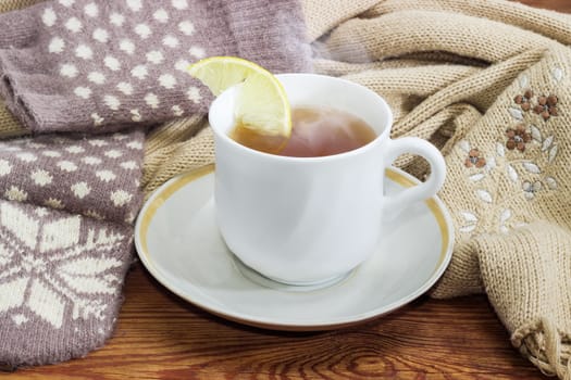 White cup of black tea with lemon on a background of women's woolen hybrid mittens and knitted scarf closeup
