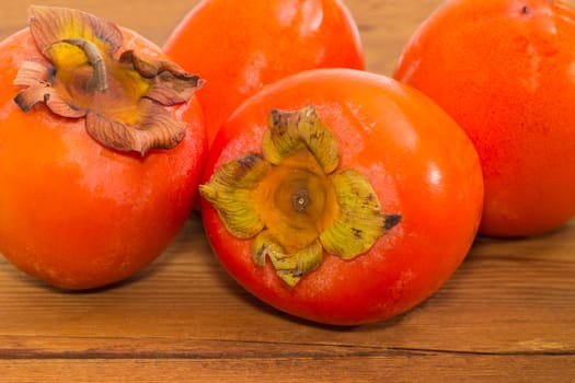 Several ripe fresh persimmons on an old wooden surface closeup
