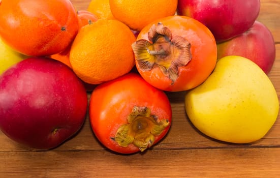 Pile of ripe fresh persimmons, apples and mandarin oranges on an old wooden surface closeup
