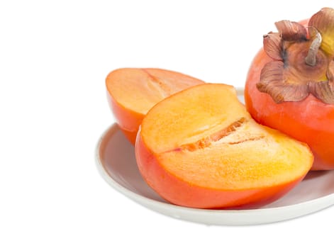 Fragment of whole ripe fresh persimmon and cut in half of a persimmon on saucer closeup on a light background
