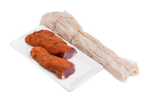 Two pieces of dried pork tenderloin on a rectangular dish and beside it dried pork tenderloin wrapped in parchment paper on a light background 
