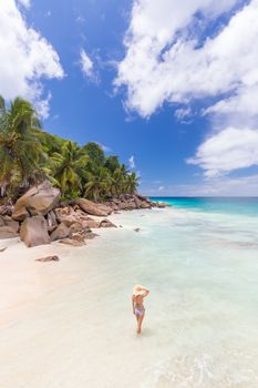 Woman wearing retro striped bikini and beach hat, enjoying amazing view on Anse Patates beach on La Digue Island, Seychelles. Summer vacations on picture perfect tropical beach concept.