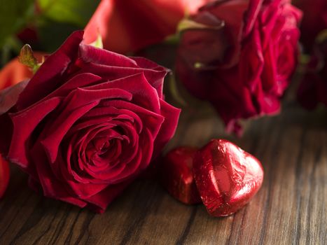 Chocolate hearts, red roses bouquet with red ribbon on dark wooden table