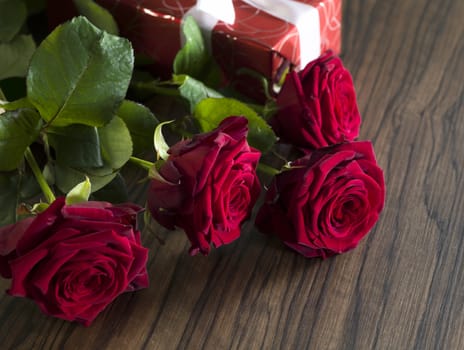 Gift box with a white ribbon and a red roses bouquet on a wooden table