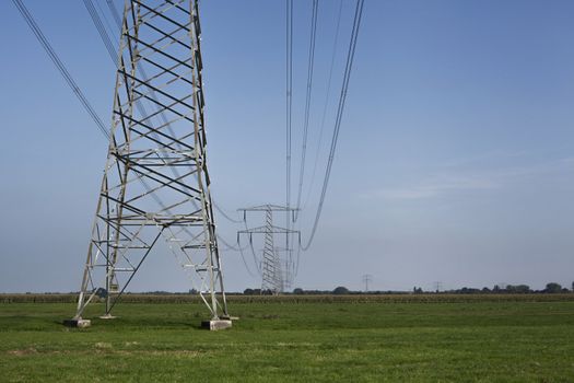 High voltage electrical transmission towers electricity pylons and power lines on green field