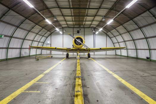 Vintage old yellow war plane inside of a clean empty hangar
