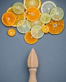 Mixed fresh citrus fruits and wooden juicer for summer citrus juice. Fresh citrus fruits sliced lime,orange and lemon on dark gray background flat lay.