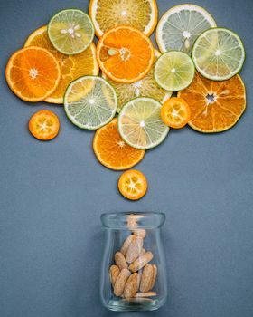 Healthy foods and medicine concept. Bottle of vitamin C and various citrus fruits. Mixed citrus fruits sliced lime,orange ,kumquat and lemon on gray background flat lay.